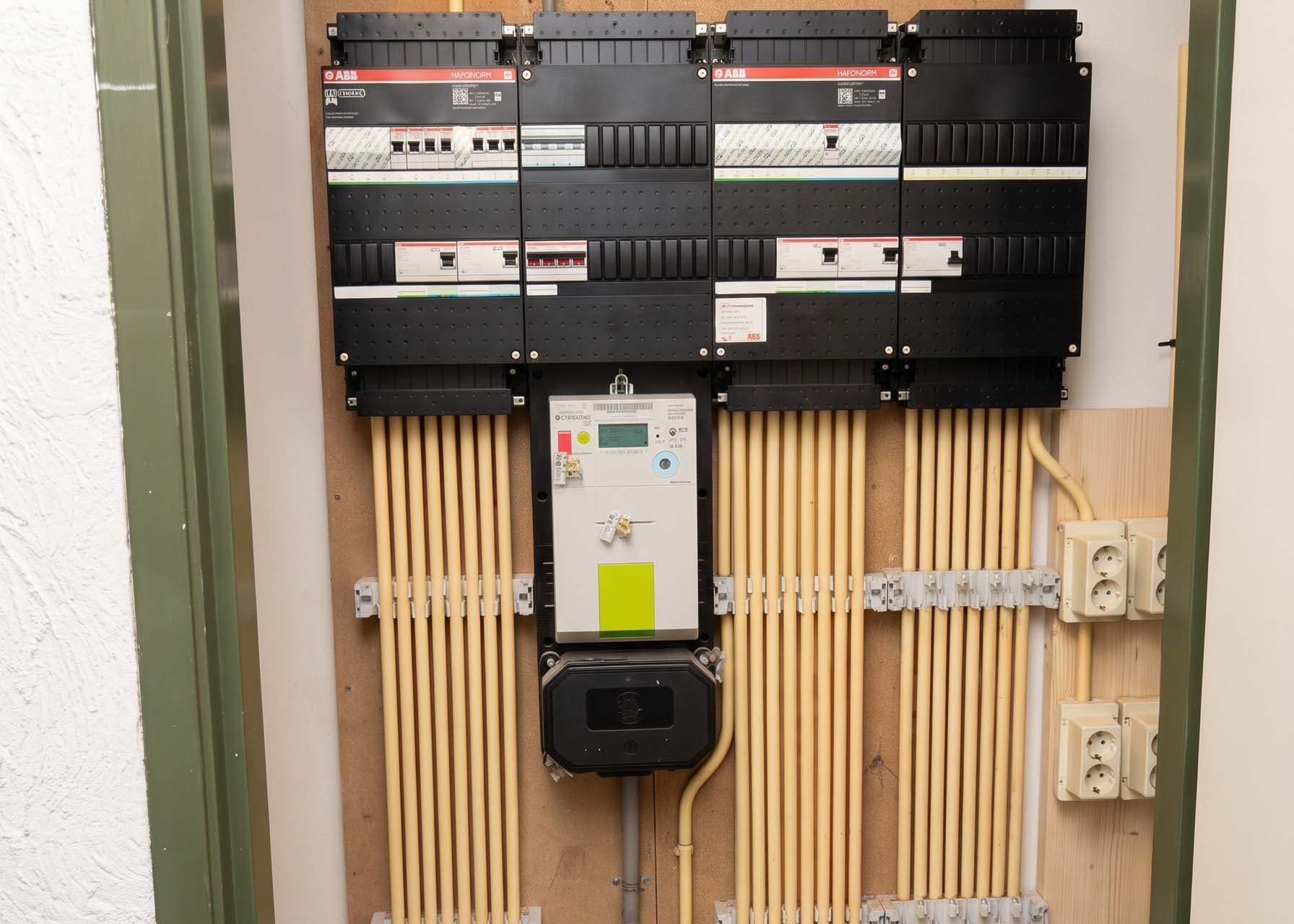 Vier afgemonteerde ABB-verdeelkasten in een meterkast, met de slimme meter ertussen en de installatiebuizen in strakke rijen langs de wand naar beneden.